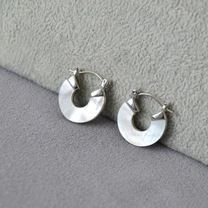 Boucles d'oreilles créoles en argent avec nacre irisée posées sur un support en peluche