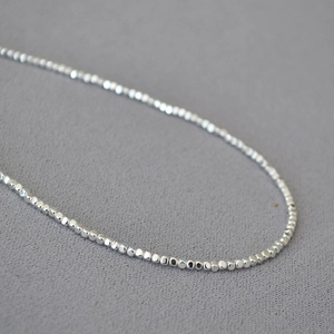 Gros plan de perles d'argent facettées étincelantes sur un collier ras du cou minimaliste fin
