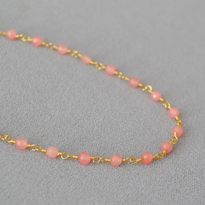 Gros plan d'une chaîne dorée avec des perles de pierre naturelle rose translucide