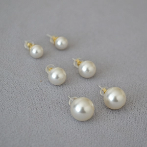 Close-up of three pairs of white pearl earrings with gold studs and silicone backs