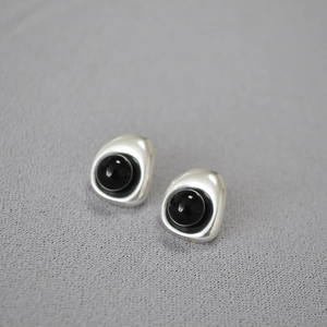 Detailed macro view of silver baroque earrings with polished black onyx-like inlay
