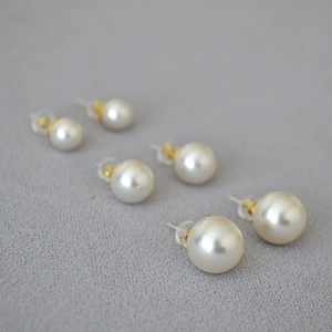 Detailed macro view of three pairs of cream pearl stud earrings with gold pins and soft glow