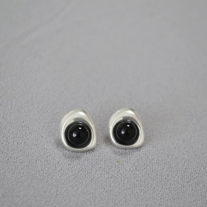 Macro shot of silver irregular organic earrings with black beads on grey fabric