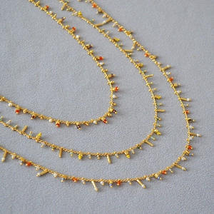 Close-up of gold chain necklaces with colorful rice beads and cylindrical charms