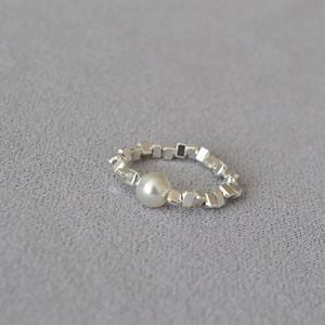 Macro detail of elastic ring featuring a white pearl and irregular silver geometric beads