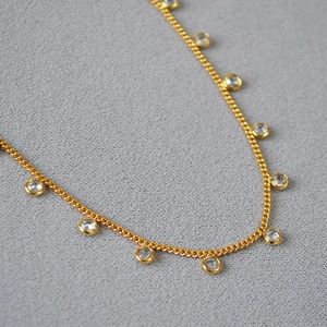 Detail of gold-plated brass necklace featuring multiple clear round cubic zirconia pendants