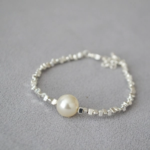 Detail view of irregular silver beads and a champagne pearl on a minimalist bracelet