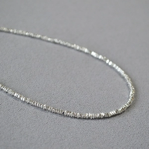 Détail macro du collier en perles d'argent facettées avec éclat métallique et texture fine