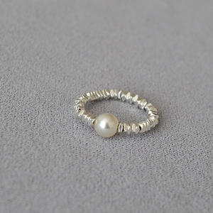 Minimalist silver irregular textured ring with a lustrous round pearl on a grey fabric