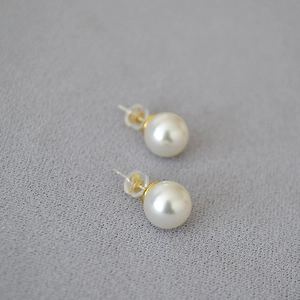Classic round white pearl stud earrings with golden 925 silver posts on grey fabric