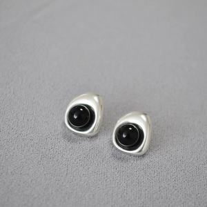 Detailed close-up of baroque style silver earrings with a black polished gemstone center