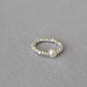 Detailed close-up of a faceted silver bead ring with a white pearl on grey fabric