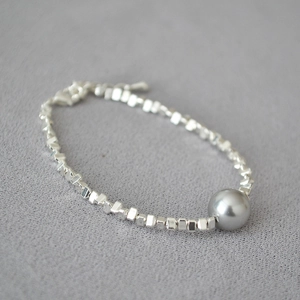 Detailed shot of irregular silver beads and a gray pearl on a minimalist bracelet