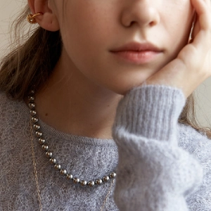 Detail of layered jewelry featuring a twisted gold ear cuff and grey pearl necklace