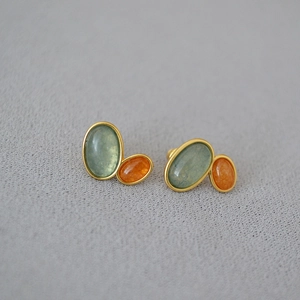Detail of vintage brass earrings with green and orange gemstones on grey fabric