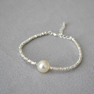 Detailed macro shot of a white pearl centerpiece on a faceted silver bead bracelet
