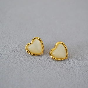 Vue détaillée des boucles d'oreilles cœur dorées avec bordure festonnée et œil de chat