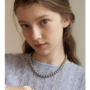 Lustrous round grey pearl necklace layered with a thin gold chain on a soft purple sweater