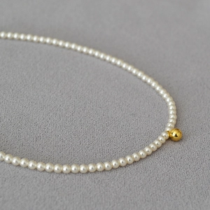 Collier élégant de perles françaises avec une perle dorée centrale sur tissu gris
