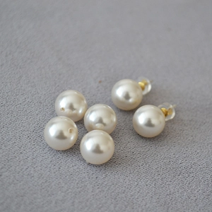 Macro shot of 925 silver pearl stud earrings with golden pins on grey fabric