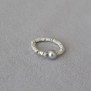 Macro detail of elastic silver faceted bead ring with a single grey pearl accent