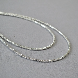 Gros plan sur un collier minimaliste en perles argentées avec texture métallique polie