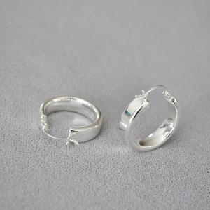 Boucles d'oreilles créoles argentées polies avec fermoir de sécurité sur tissu gris