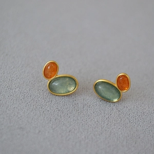 Close-up of gold-plated brass earrings with orange and turquoise oval gemstone inlays