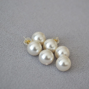 Close-up of elegant round white pearl earrings with golden pins and silicone backs
