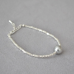Detailed macro view of irregular silver beads and a large dark grey pearl on the bracelet