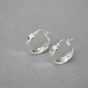 Boucles d'oreilles créoles argentées minimalistes avec finition polie sur fond texturé