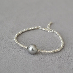 Detail of irregular silver beads and a gray pearl bracelet with minimalist texture