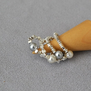 Detail of three minimalist beaded rings with silver cubes and pearls on a wood stand