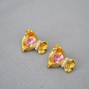 Vue macro de boucles d'oreilles dorées avec zircon rose et petites perles blanches