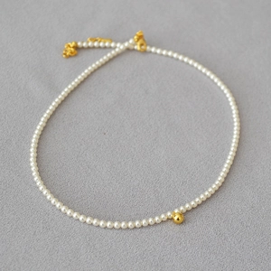 Détail d'un collier de perles délicat avec une perle dorée centrale et un fermoir mousqueton