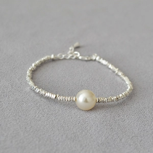Macro detail of silver bead bracelet with a lustrous freshwater pearl on a textured grey surface