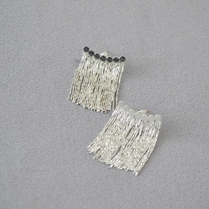 Détail de boucles d'oreilles à pampilles argentées avec barre à texture ondulée