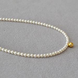 Détail d'un collier de perles élégant avec perle dorée polie sur un fond de tissu gris