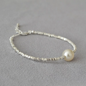Close-up of beaded silver bracelet with a central pearl and adjustable lobster clasp