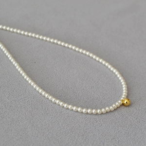 Vue macro d'un collier de perles délicates avec une bille d'or polie sur tissu texturé