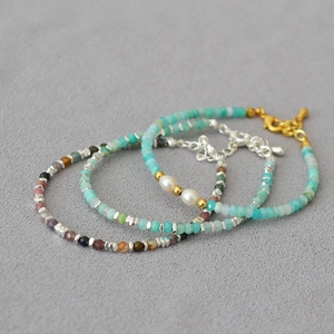 Makrofoto von geschichteten Armbändern aus Amazonit, Perlen und Turmalin mit goldenen Details