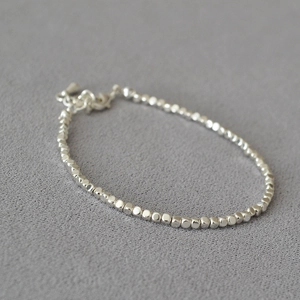 Detailed shot of irregular silver beads and pearls on minimalist textured fabric