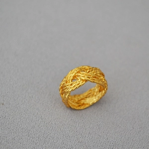 Macro shot of gold-plated braided wide ring with detailed interwoven brass texture
