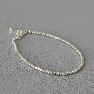 Detailed shot of irregular silver beaded bracelet with lobster clasp on grey fabric