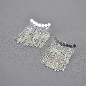 Vue macro de boucles d'oreilles à pampilles argentées sur cuir gris, texture métallique chic