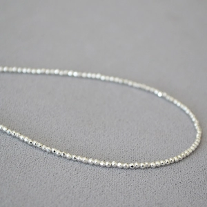 Macro shot of minimalist silver faceted beaded necklace with polished metallic shine