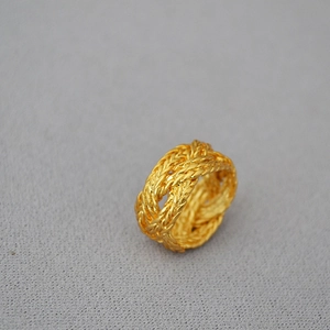 Detailed view of wide braided gold ring with intricate twisted metal texture on gray fabric