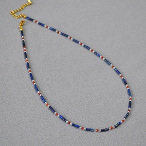 Détail du collier avec perles de lapis-lazuli et accents d'agate rouge sur tissu gris