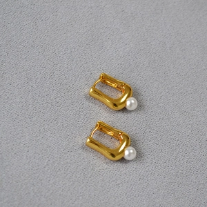 Boucles d'oreilles dorées en forme de U avec perle nacrée sur un fond gris neutre