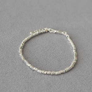 Detailed macro view of irregular silver beads and lobster clasp on a minimalist bracelet